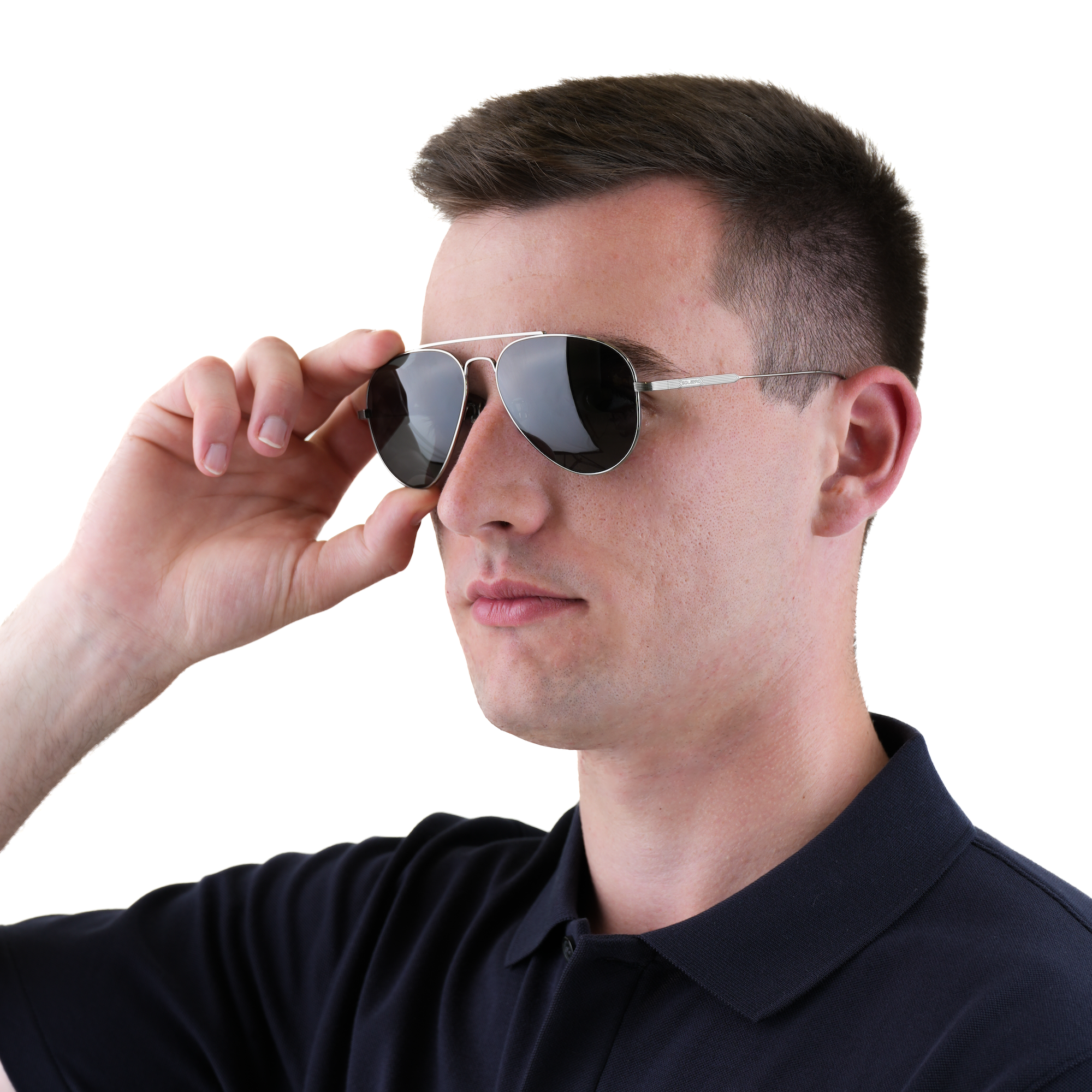 A man wearing a black polo shirt and aviator sunglasses with a thin silver metal frame, adjusting the glasses with his right hand against a solid white background.