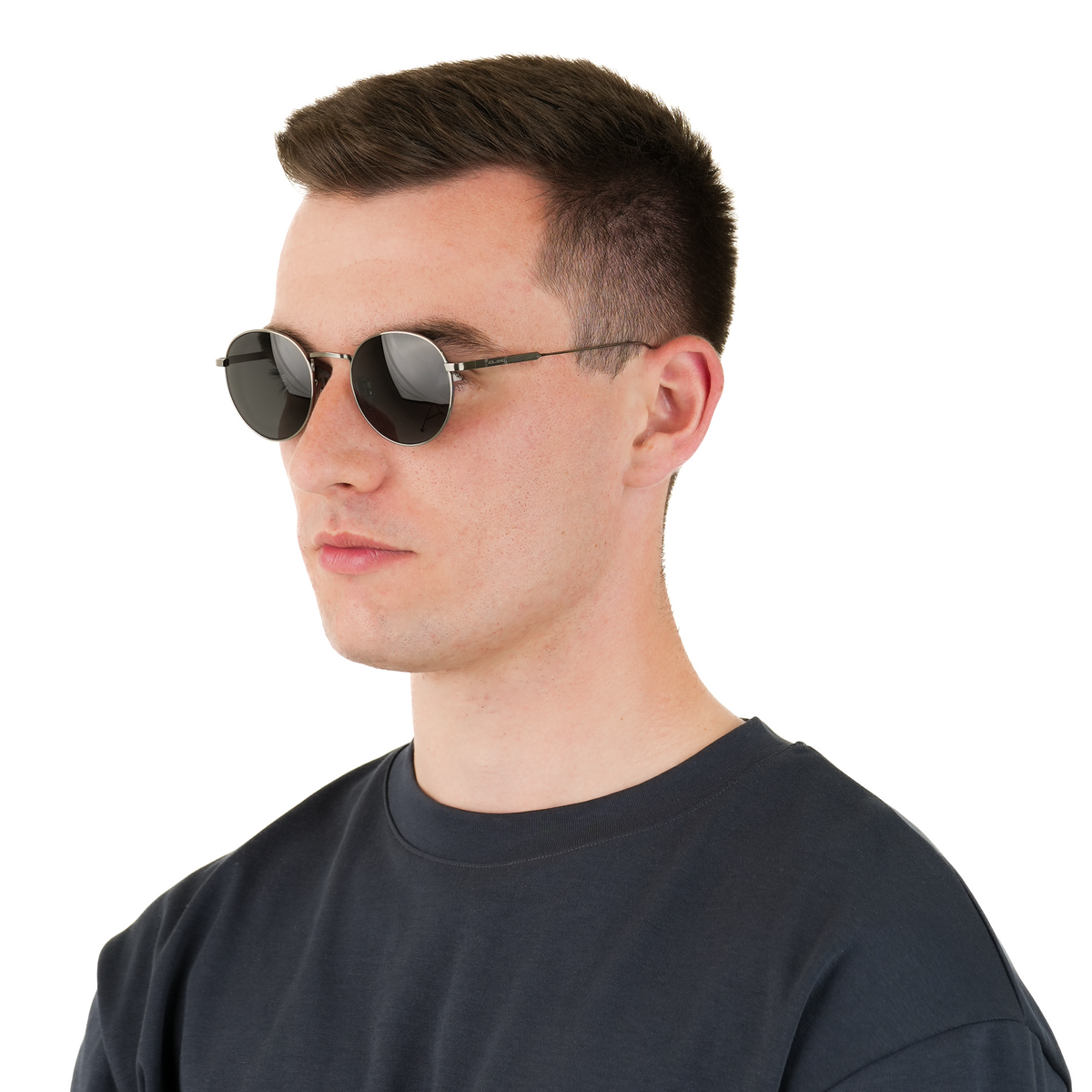 A man in profile wearing round dark sunglasses with thin metallic frames and a dark crew-neck t-shirt, photographed against a solid white background.