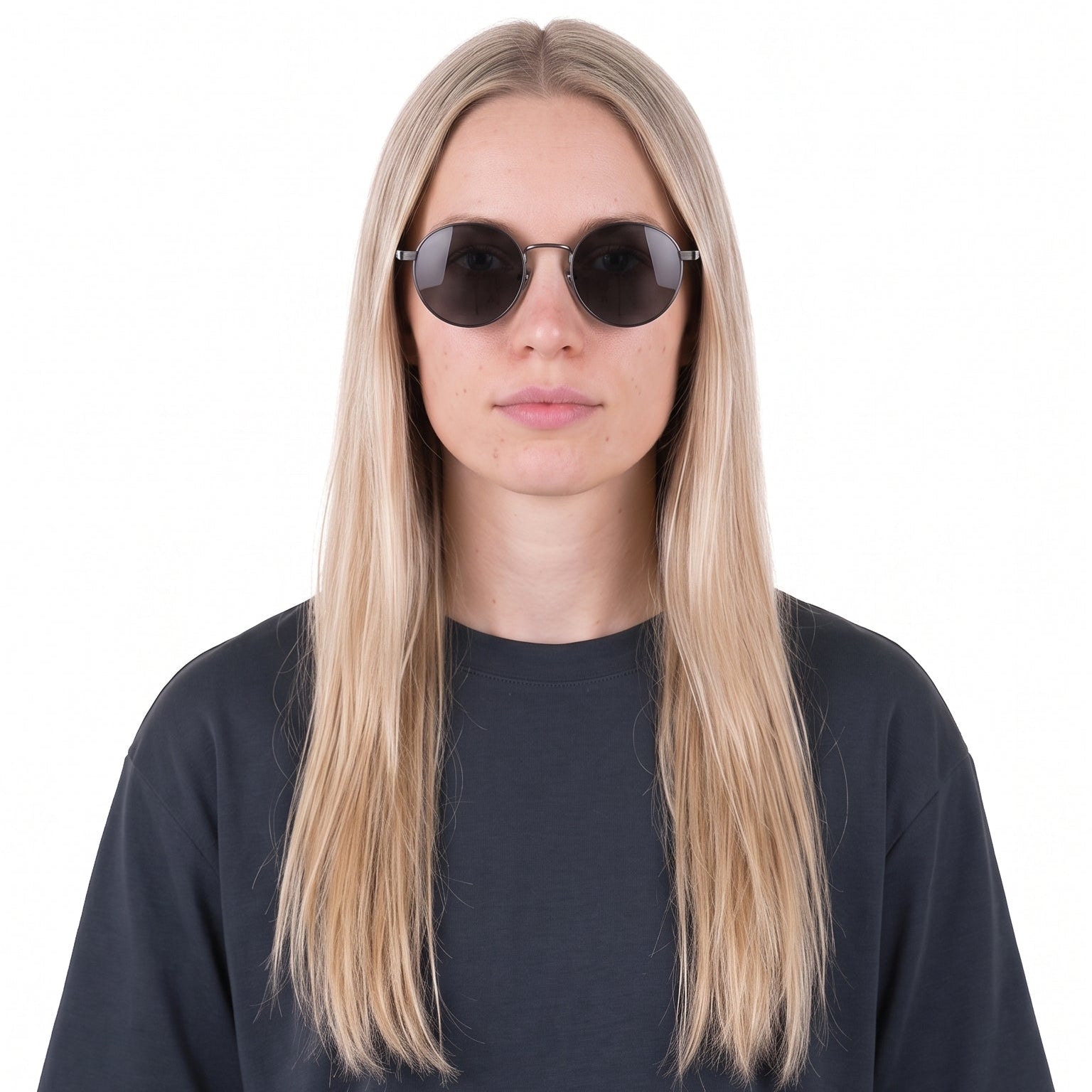 A woman with long blonde hair wearing round black sunglasses and a dark charcoal gray oversized t-shirt, shown from the chest up against a plain white background.